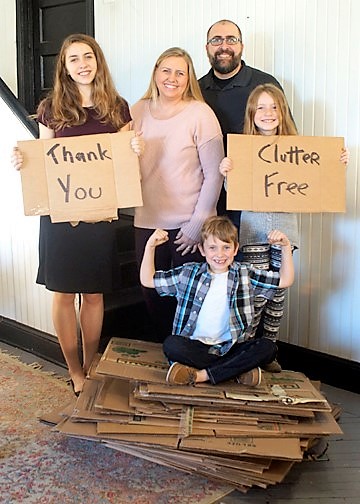 family standing next to stack of cardboard boxes while holding cardboard thank you sign